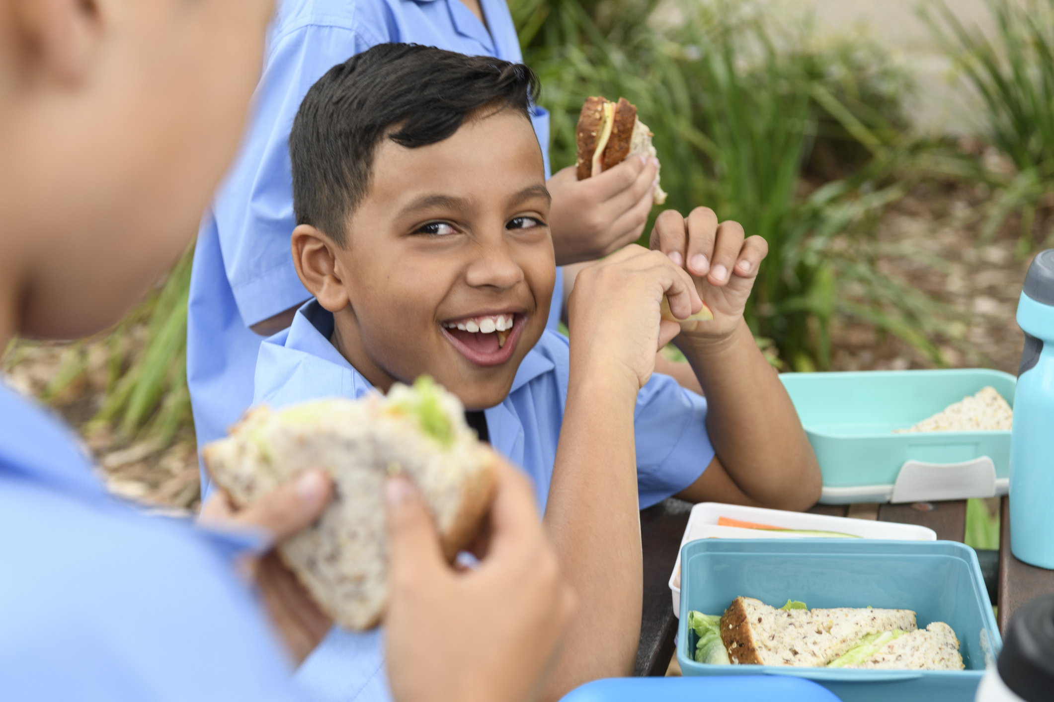 Ethnic boy eating packed lunch out side with school friends