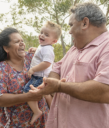 Portrait of three generation Aboriginal family - Grandparents holding little boy, mother smiling towards camera, grandfather clapping